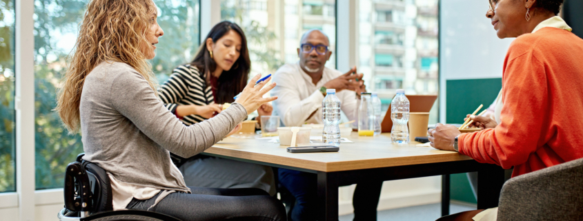 A diverse group of professionals, including a woman using a wheelchair, engaged in a workplace discussion. The image represents inclusive work environments and the evolving landscape of DEI initiatives, aligning with the challenges employers face in maintaining compliance while fostering diversity and respect in the workplace.