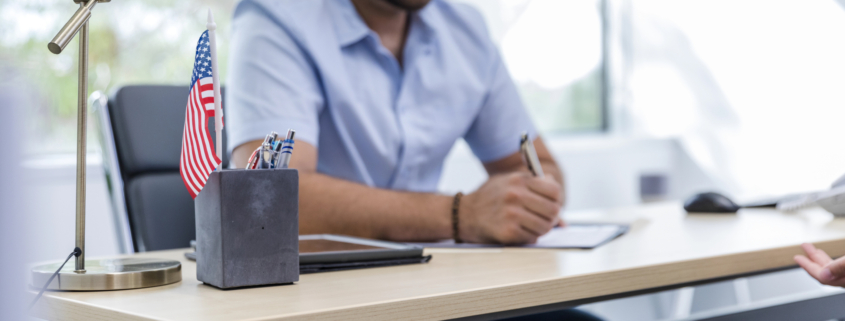 An employer verifying an employee's identity and work authorization, completing Form I-9 as part of the hiring process. The desk setup includes a small American flag, symbolizing compliance with U.S. employment eligibility requirements.
